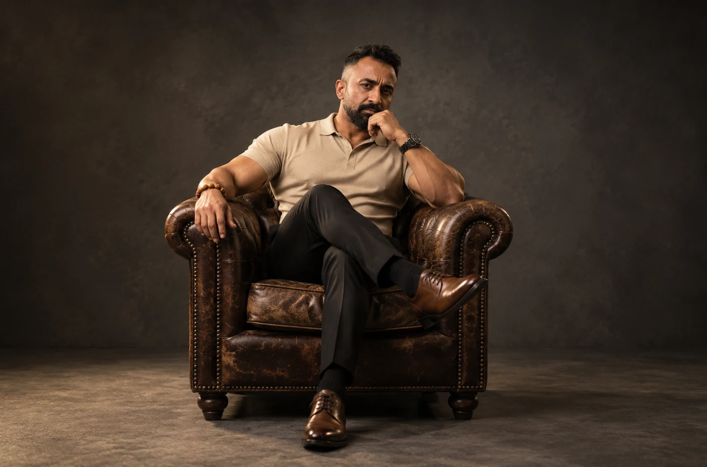 Satyajit Dasgupta seated in a leather armchair against a warm textured ground.